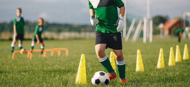 Kinderfußballerin dribbelt durch Kegel. Junge in Fußballuniform üben mit Ball. Kind kickt Ball auf Gras. Junger Athlet verbessert seine Dribbelkünste - Foto, Bild