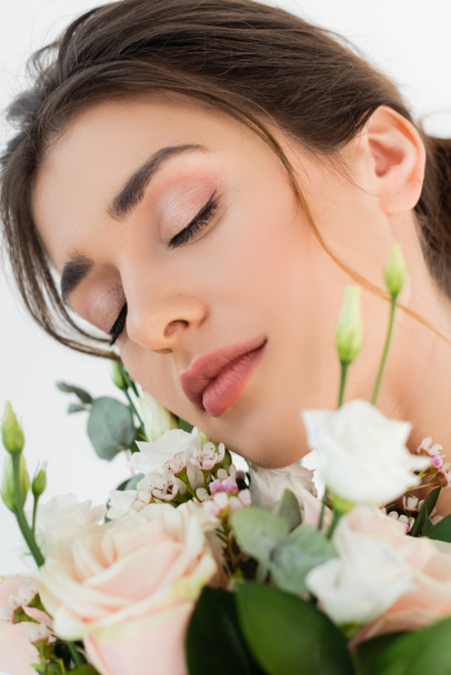 vue rapprochée de jeune femme avec maquillage naturel près du bouquet de mariage isolé sur blanc - Photo, image