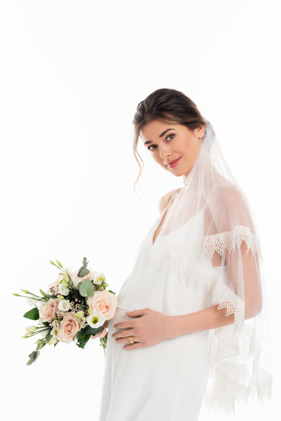 беременная невеста держит свадебный букет, глядя на камеру, изолированную на белом - Фото, изображение
