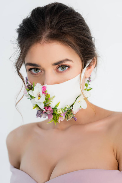 Sağlık maskeli, çiçekli esmer kadın gri kameraya bakıyor. - Fotoğraf, Görsel