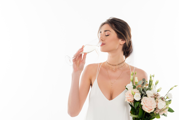 giovane fidanzata che tiene bouquet da sposa mentre beve champagne isolato su bianco - Foto, immagini