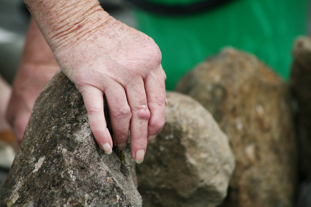 Viver com séries de dor. Mãos de uma mulher idosa com artrite reumatoide movendo pedras no jardim
 - Foto, Imagem