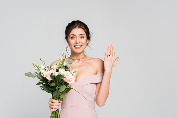örömteli nő mutatja jegygyűrű, miközben a gazdaság virágok elszigetelt szürke - Fotó, kép