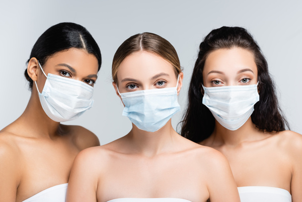 νεαρές πολυεθνικές γυναίκες σε μπλούζες με γυμνούς ώμους και ιατρικές μάσκες που απομονώνονται σε γκρι - Φωτογραφία, εικόνα