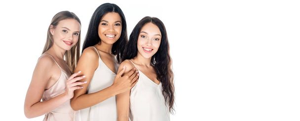 fröhliche interrassische Frauen in Kleidern, die isoliert auf weißem Banner lächeln - Foto, Bild