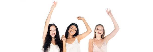 excited interracial women in dresses standing with raised hands isolated on white, banner - Photo, Image