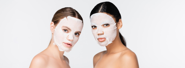 young interracial women in moisturizing sheet masks isolated on white, banner - Photo, Image