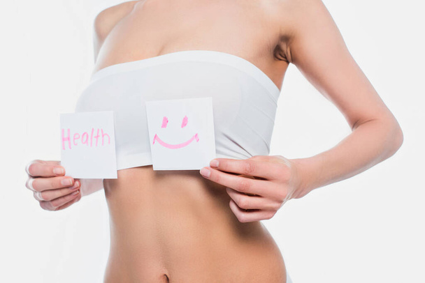 Vista cortada de jovem mulher em sutiã segurando cartões com letras de saúde e sinal de sorriso isolado no branco  - Foto, Imagem