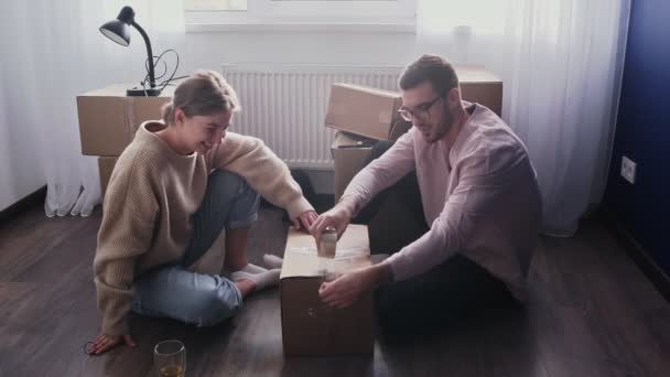 Joyeux couple emballant des boîtes en carton, préparez-vous à déménager, famille assise sur le sol dans le salon le jour du déménagement - Séquence, vidéo