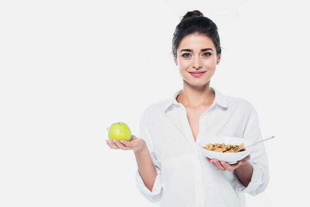 Smiling woman holding fresh apple and bowl of cereals isolated on white  - Photo, Image