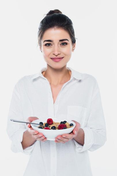 Mujer sonriente sosteniendo tazón de cereales y bayas aisladas en blanco  - Foto, imagen