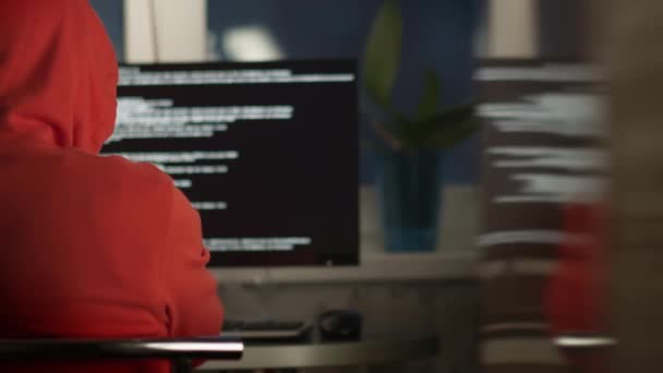 un homme dans une hotte travaille à un écran d'ordinateur à la maison, vue arrière - Séquence, vidéo