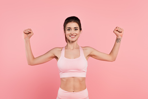 Cheerful sportswoman showing muscles isolated on pink  - Photo, Image
