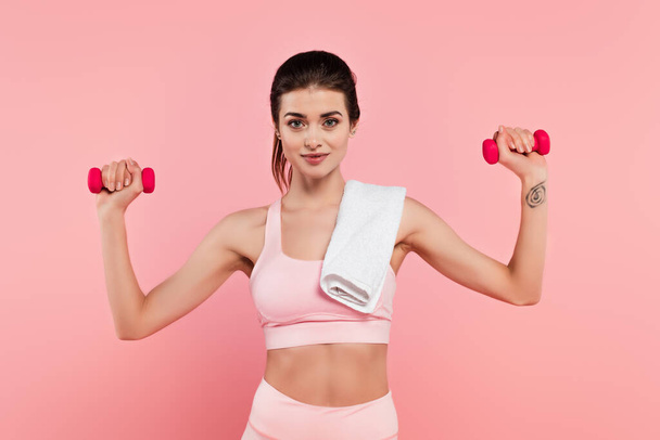 Young sportswoman with towel exercising with dumbbells isolated on pink  - Photo, Image