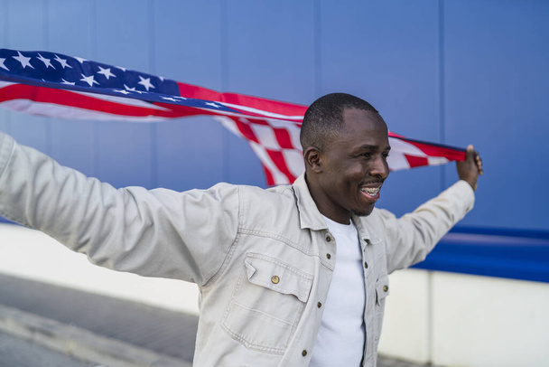 A closeup shot of a smiling black male holding the flag of the USA - Zdjęcie, obraz