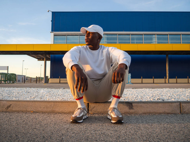 A black Spanish male in a white hat sitting on a curb - Foto, immagini