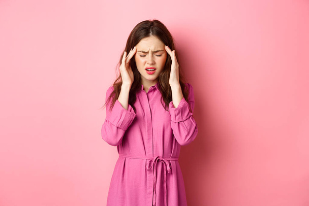 Frau mit Kopfschmerzen, Schläfen berühren und Stirnrunzeln, Migräne, Schwindel, Kopfschmerzen vor rosa Hintergrund - Foto, Bild