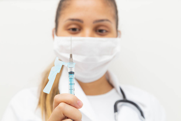 Γυναίκα γιατρός κοιτάζει επίμονα τη βελόνα μιας σύριγγας με εμβόλιο. - Φωτογραφία, εικόνα