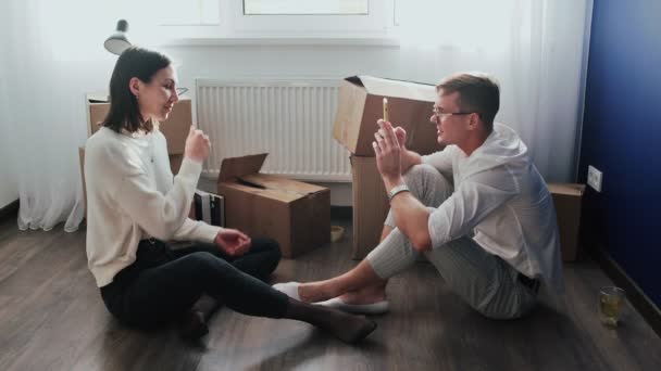 Happy couple relaxes after moving in a new home. Couple sits on floor and celebrates their moving in a new home. Man takes a photo of his wife with keys - Footage, Video