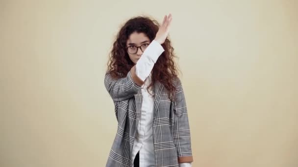 The responsible young woman, with folded hands, says stop, safety is at the forefront. Cretaceous in gray jacket and white shirt, with glasses posing isolated on a beige background in the studio. - Footage, Video