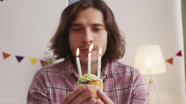 Camera pov of young man in party cap blowing candles on holiday cake, celebrating birthday online at home - Footage, Video