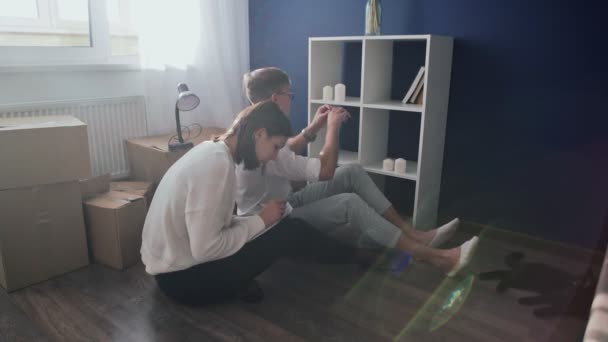 Glückliches Paar bereitet sich auf Umzug vor, Familie sitzt am Umzugstag auf dem Fußboden im Wohnzimmer - Filmmaterial, Video