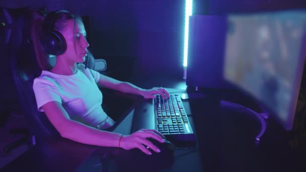ヘッドフォンで若い集中ゲーマーの女性は、ゲームクラブでコンピュータに座ってシューティングゲームをプレイ - 映像、動画