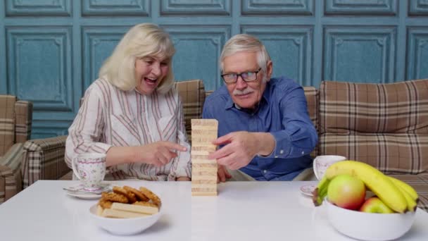 Starší pár v důchodu tráví čas spolu hrát hru s dřevěnými bloky na stole v obývacím pokoji - Záběry, video