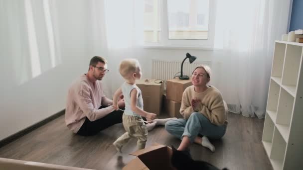 Happy couple relaxes after moving in a new home. Couple sits on floor, little kid kisses his mother - Footage, Video