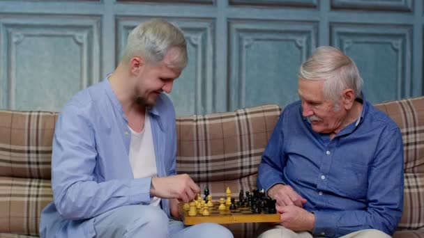 Happy different male generations family of senior father and adult son or grandson playing chess - Footage, Video