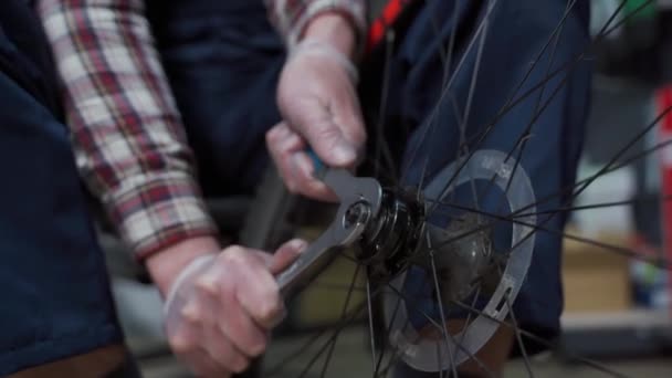 Mécanicien masculin travaillant dans un atelier de réparation de vélos, mécanicien réparant le vélo à l'aide d'un outil spécial, portant des gants de protection. Jeune militaire attrayant fixant clients roue de vélo à son propre atelier - Séquence, vidéo