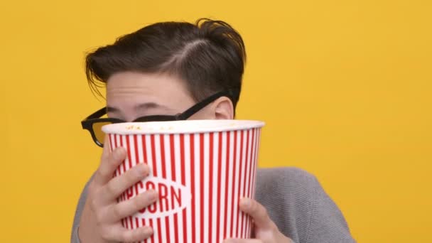 Niño viendo película de terror escondiéndose detrás de palomitas de maíz cubo, fondo amarillo - Imágenes, Vídeo