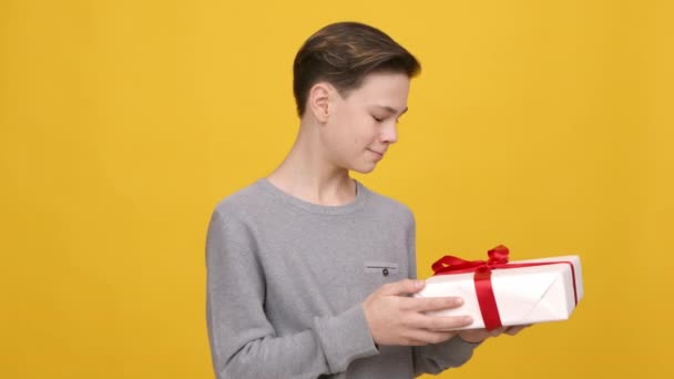 adolescent garçon donner enveloppé cadeau boîte pour caméra, fond jaune - Séquence, vidéo