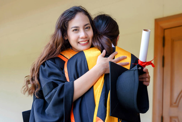 A universidade asiática graduados em vestido de graduação e um boné de papelão com um certificado de grau na mão celebrando a realização da educação na cerimônia de início. Parabéns às formaturas - Foto, Imagem