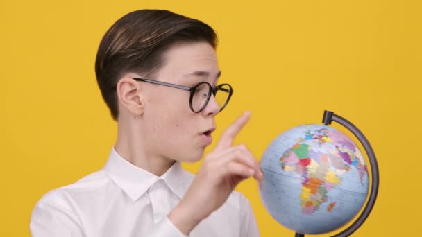 Schoolboy Holding Earth Globe δείχνοντας Δάχτυλο Επιλέγοντας Προορισμό, κίτρινο φόντο - Πλάνα, βίντεο