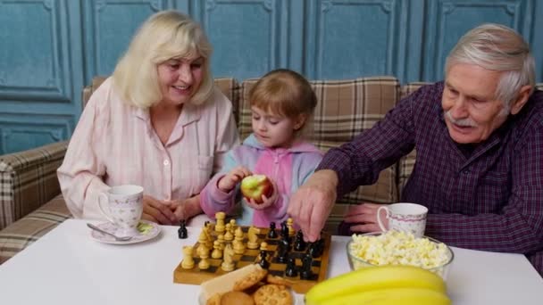 Érett nagymama nagypapa a gyermek lány unokája sakkozik játék az asztalon a szobában - Felvétel, videó