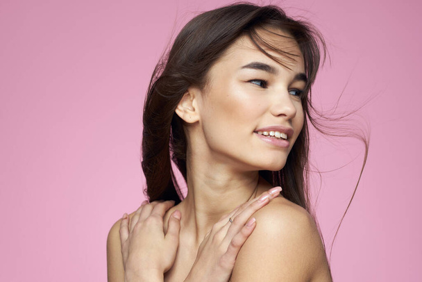 Brunette with bare shoulders holding her hair clean skin pink background - Foto, immagini