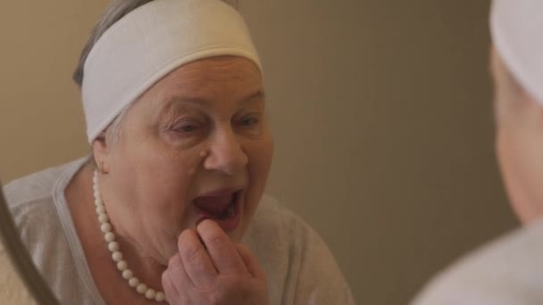 Ritratto di donna anziana davanti allo specchio che applica il rossetto - Filmati, video