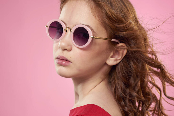 Girl with curly hair dark round glasses fun red dress pink background - Foto, imagen