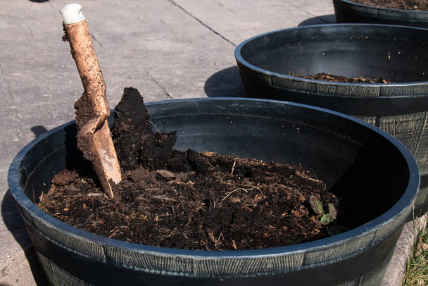 Een troffel halverwege begraven in de bovenste grond en meststof in een zwarte houten pot naast andere houten potten op gouden uur in Ontario, Canada. Close-up.   - Foto, afbeelding