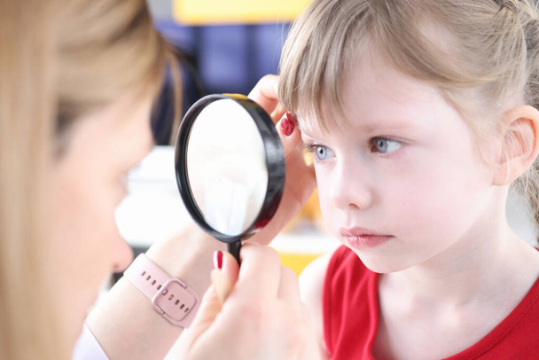 Lääkäri tutkii silmä pikkutyttö käyttäen suurennuslasi - Valokuva, kuva