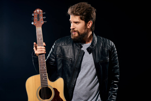 Un homme avec une guitare dans ses mains veste en cuir performance musique rock star style moderne fond sombre - Photo, image