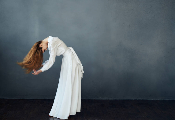 A woman in a white dress is dancing on a gray background in full growth red hair model - Photo, Image