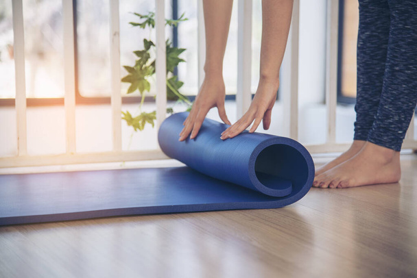 Woman hands rolled up yoga mat on gym floor in yoga fitness training room. Home workout woman close up hands rolling foam yoga gym mat. Woman barefoot home workout sportive healthy lifestyle concept - Photo, Image