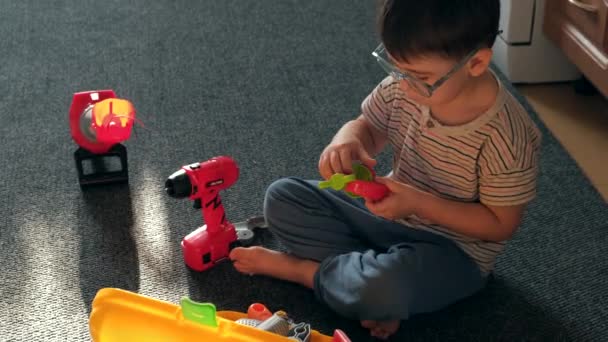 Верхний вид видео кавказского мальчика в очках, играющих на полу с конструкторскими игрушками - Кадры, видео