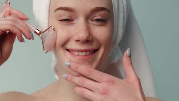 Freckled woman with ginger hair is massaging her face with a derma roller smiling at camera - Záběry, video