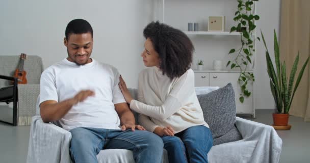 Afro-Amerikaanse man voelt stress terwijl vrouw verontschuldigen praten smeken boos man vragen om vergeving thuis, vriendin spijt consoles ondersteunt geliefde vriend zitten op de bank - Video