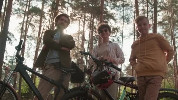Low-angle PAN medium portret met slowmo van de Kaukasische familie van drie rusten in het bos bij daglicht na fietsen samen - Video