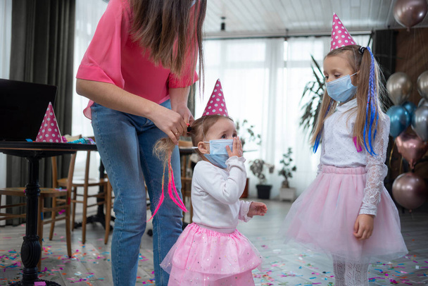 Während der Party flechtet Mama dem Mädchen die Zöpfe. Geburtstagsfeier während der Quarantäne. Kopierraum. - Foto, Bild