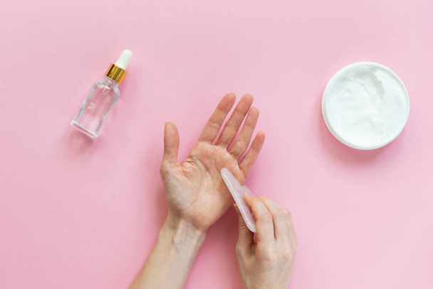 Hand massage with a gua sha scraper on a pink background. Horizontal orientation, top view. - Photo, Image